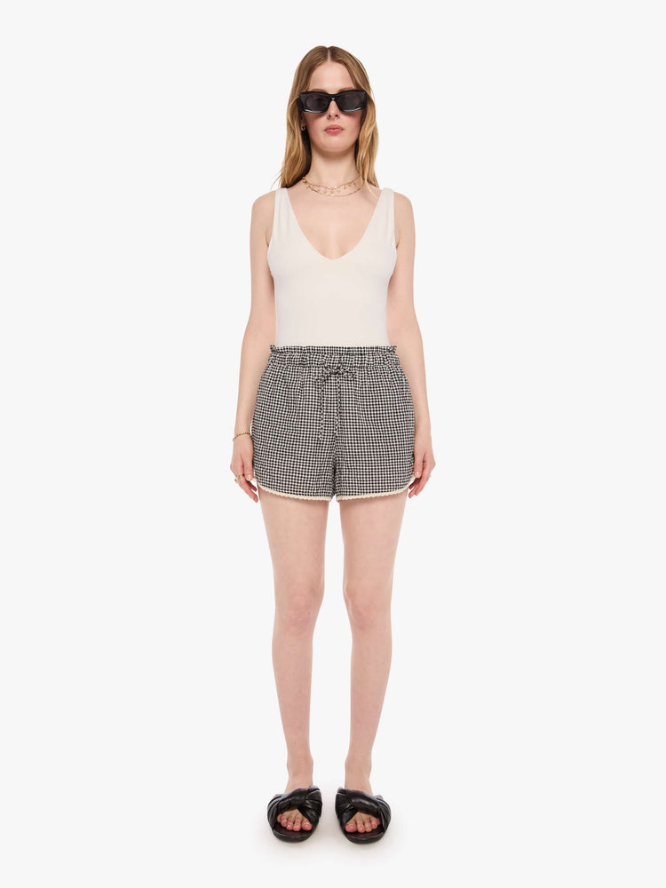 Front view of a woman in black and off white short with a drawstring waist, curved hem and a loose, flowy fit.