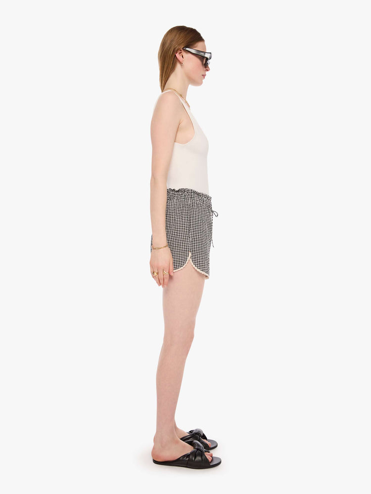 Side view of a woman in black and off white short with a drawstring waist, curved hem and a loose, flowy fit.