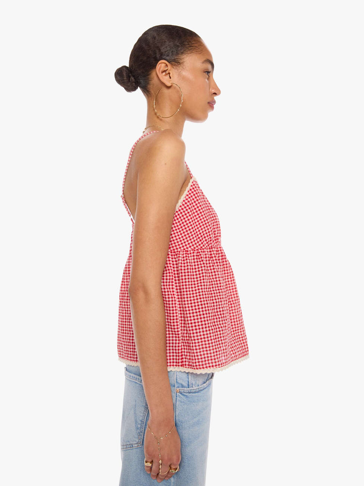 Side view of a woman in a red and off-white gingham thin spaghetti straps, a V-neck, gathered bodice and buttons down the front.
