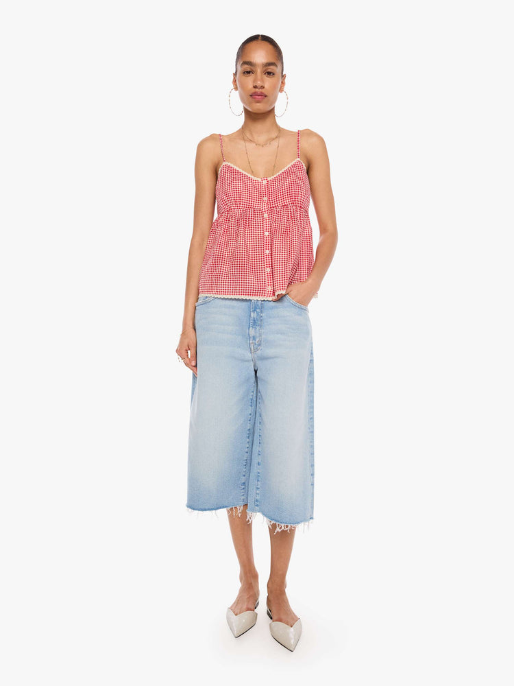 Full body  view of a woman in a red and off-white gingham thin spaghetti straps, a V-neck, gathered bodice and buttons down the front.
