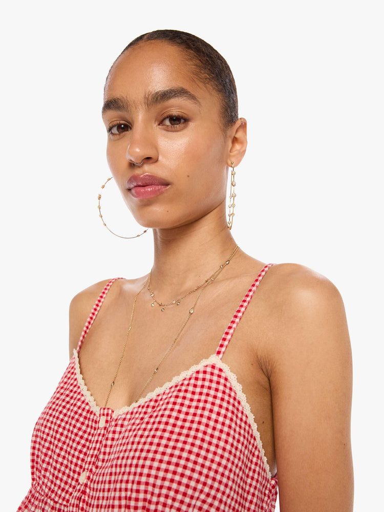 Close up  view of a woman in a red and off-white gingham thin spaghetti straps, a V-neck, gathered bodice and buttons down the front.