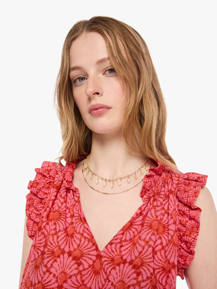 Close up view of a woman in a vneck top pink and orange graphic print, and features short, ruffled sleeves and a boxy fit.