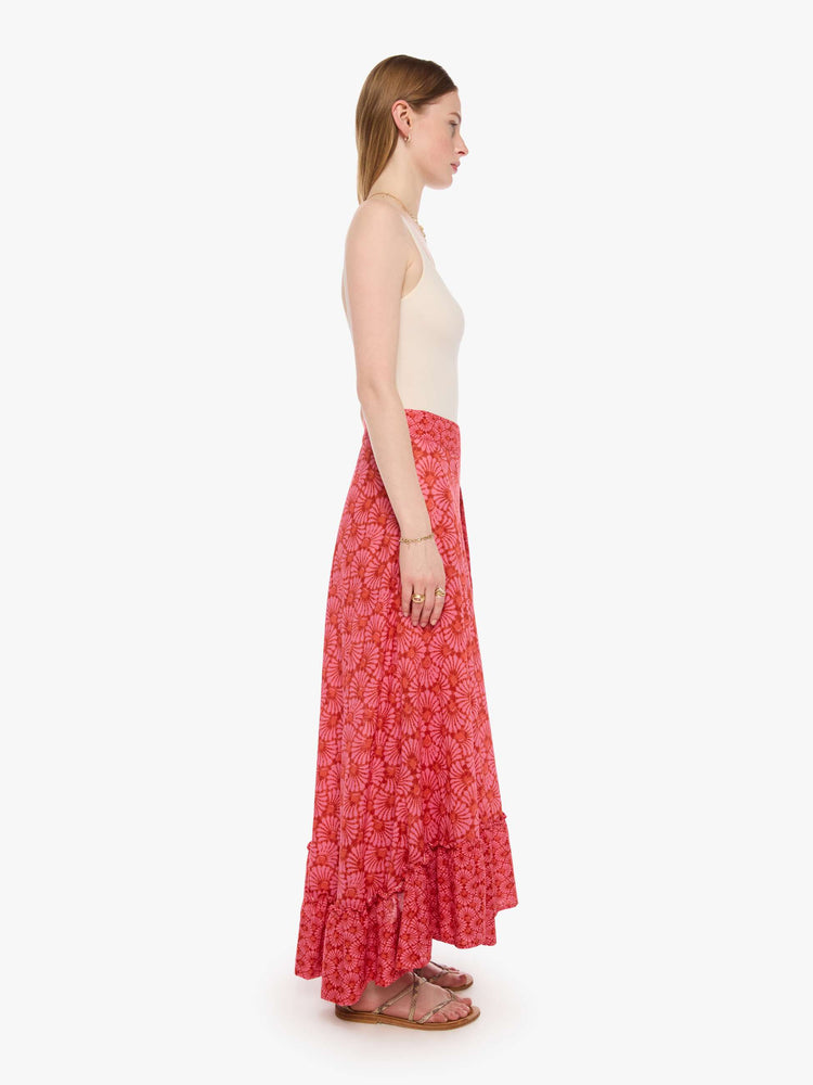 Side view of a woman in a pink and orange graphic print skirt, and features a high rise, wrap closure, ruffled hem and a loose, flowy fit.