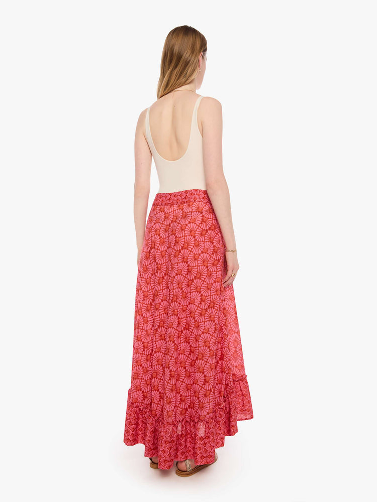 Back view of a woman in a pink and orange graphic print skirt, and features a high rise, wrap closure, ruffled hem and a loose, flowy fit.