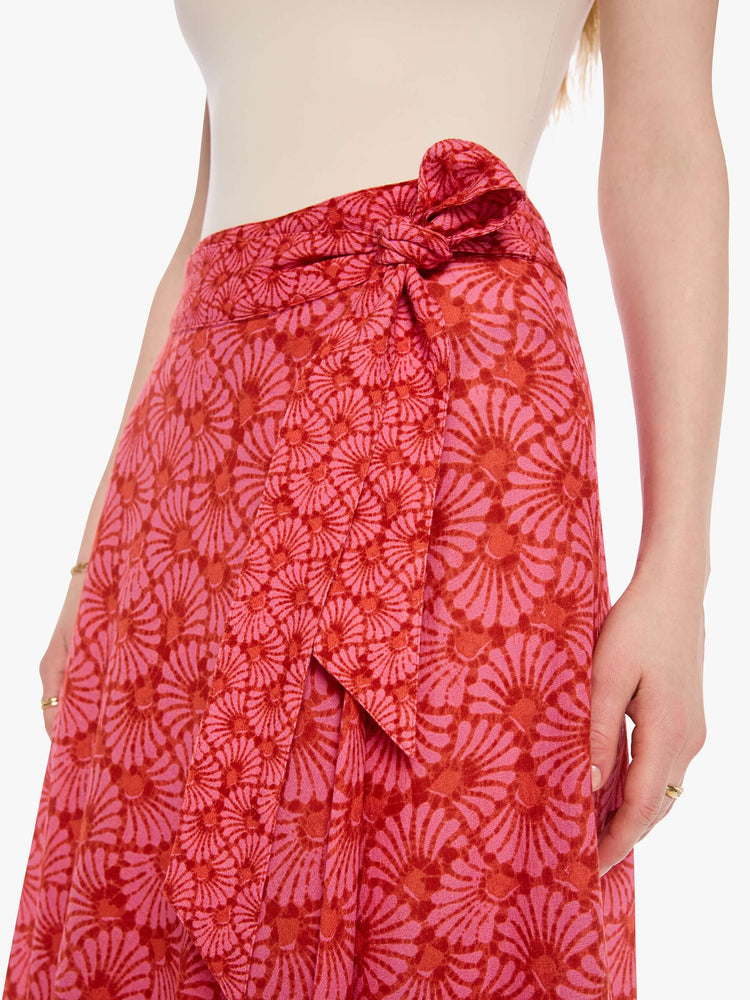 Close up view of a woman in a pink and orange graphic print skirt, and features a high rise, wrap closure, ruffled hem and a loose, flowy fit.