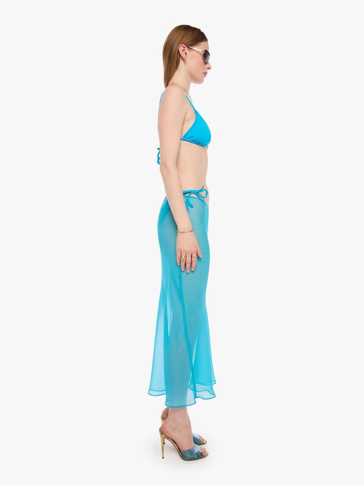 Side view of a woman in a turquoise see-through maxi skirt from SPRWMN with an elastic waist, narrow fit and ankle-length hem. 