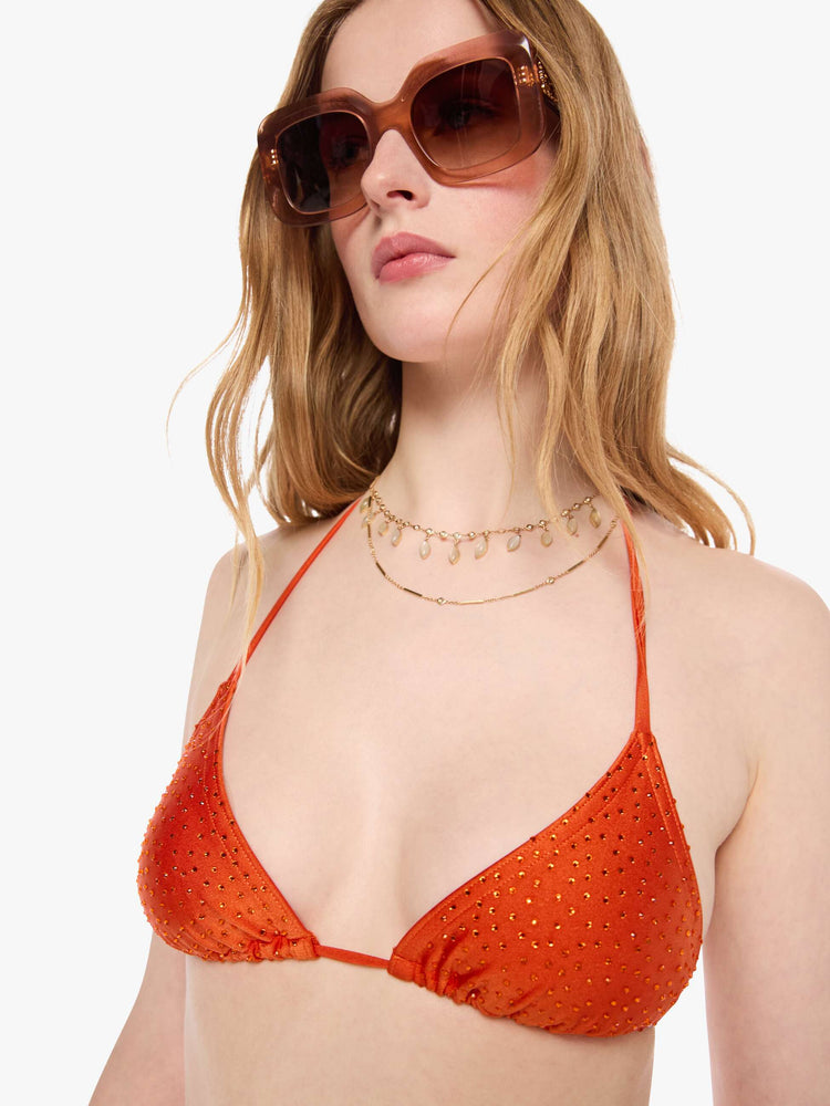 Close up  view of a woman in string bikini top from SPRWMN with decorative rhinestones throughout in orange, the bikini top has a triangle design and tie closures.