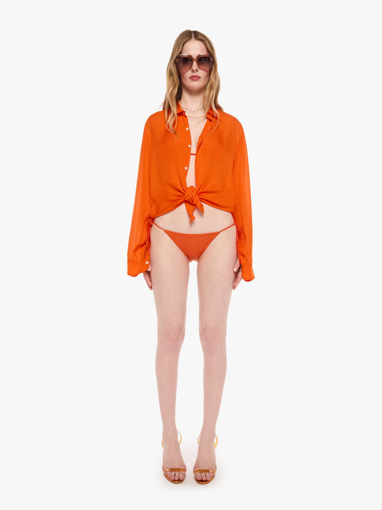 Front view of a woman in string bikini bottom from SPRWMN with decorative rhinestones throughout in orange, the bikini bottoms have a low rise and tie closures.