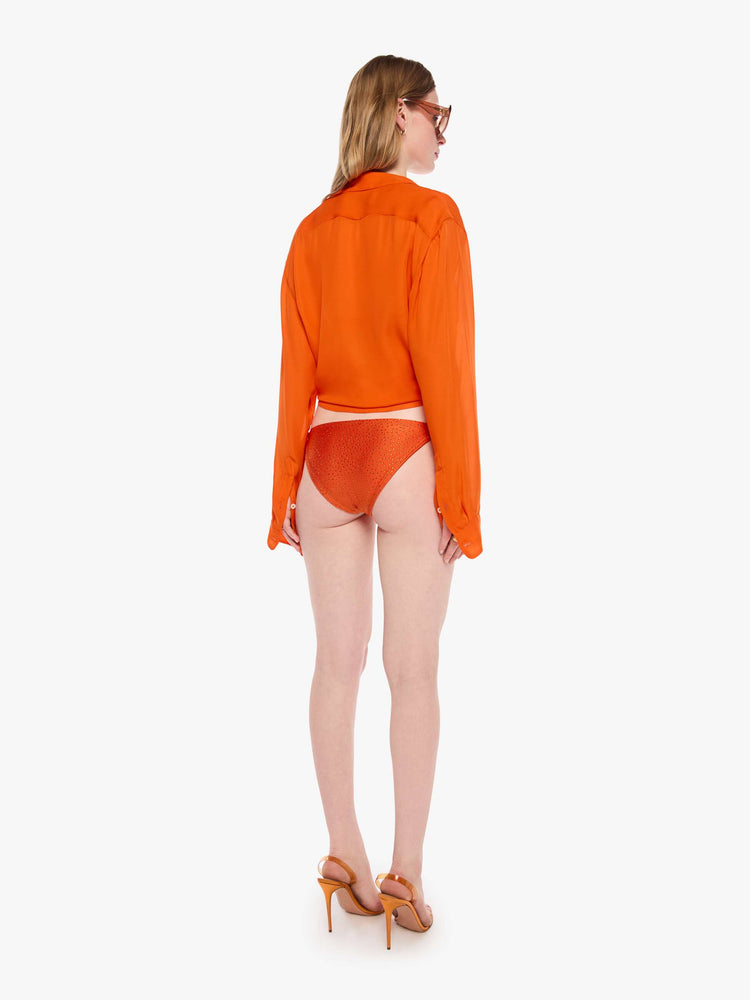 Back view of a woman in string bikini bottom from SPRWMN with decorative rhinestones throughout in orange, the bikini bottoms have a low rise and tie closures.
