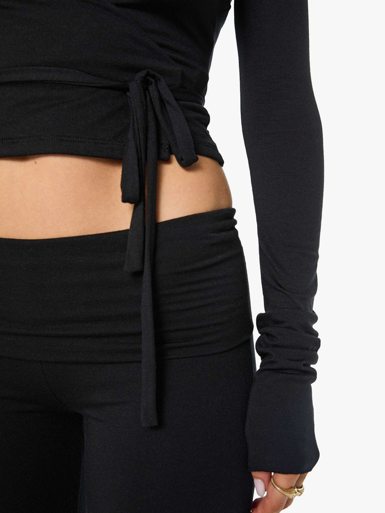 Close up view of a woman in a black top with a deep V-neck, long sleeves, a tied waist and a cropped, narrow fit.