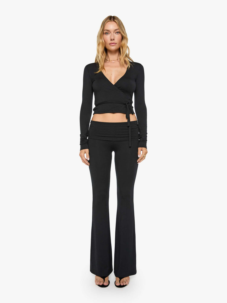 Front view of a woman in black pants with a folded waistband and a slightly cropped flared leg.