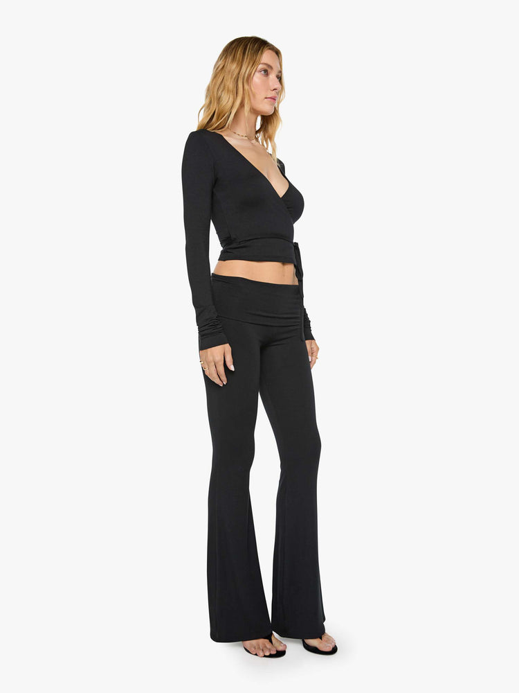 Side angle view of a woman in black pants with a folded waistband and a slightly cropped flared leg.