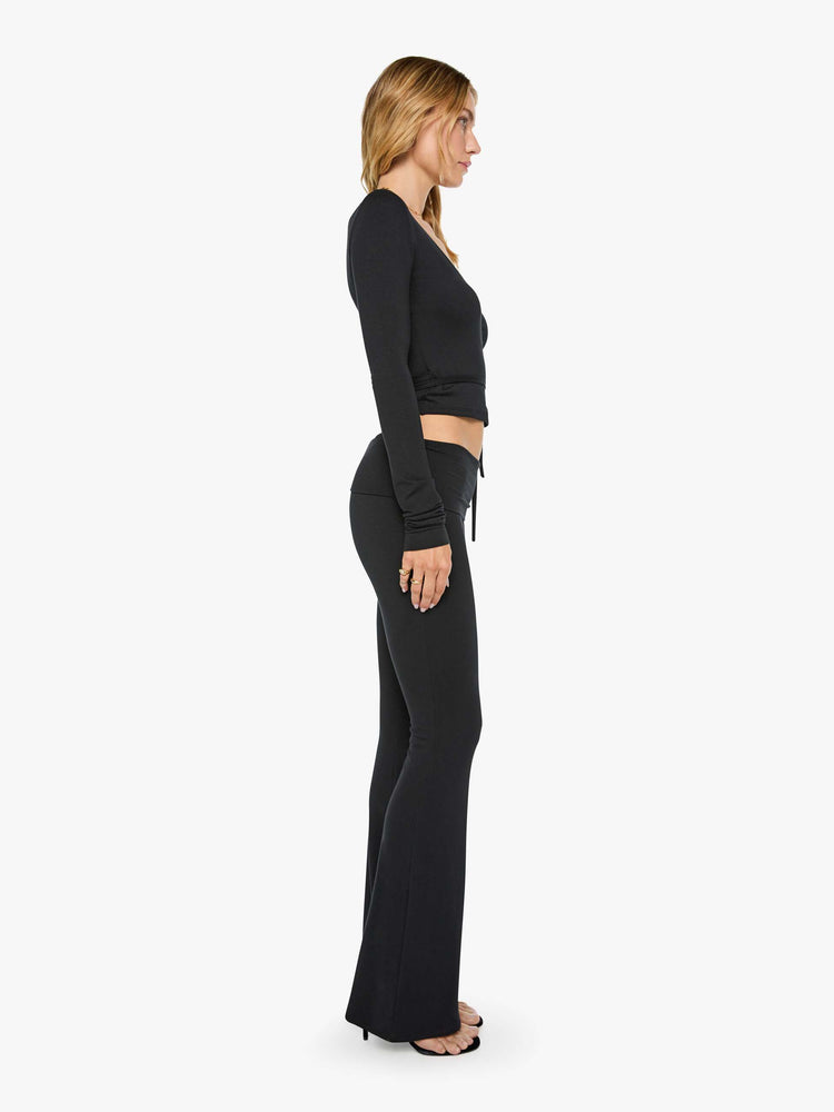 Side view of a woman in black pants with a folded waistband and a slightly cropped flared leg.