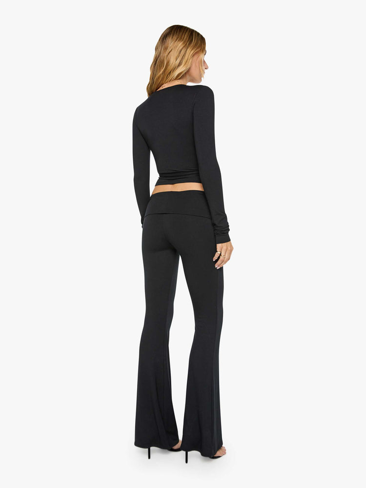 Back view of a woman in black pants with a folded waistband and a slightly cropped flared leg.