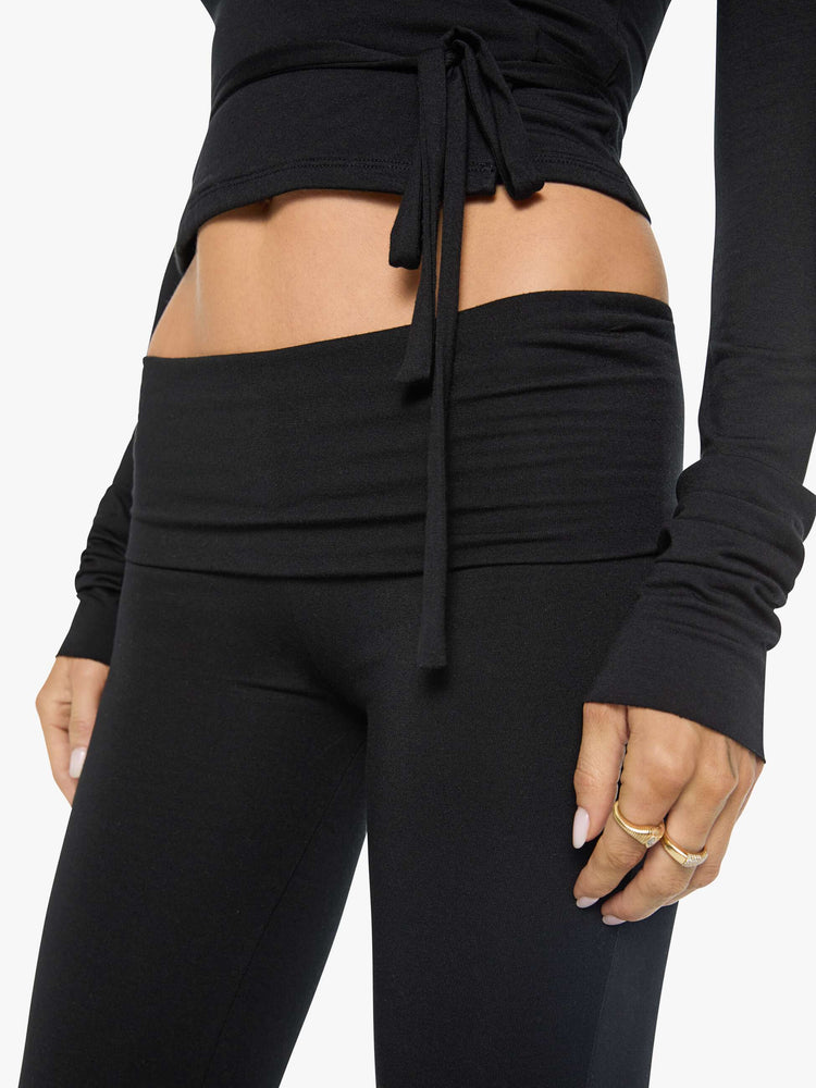 Close up view of a woman in black pants with a folded waistband and a slightly cropped flared leg.