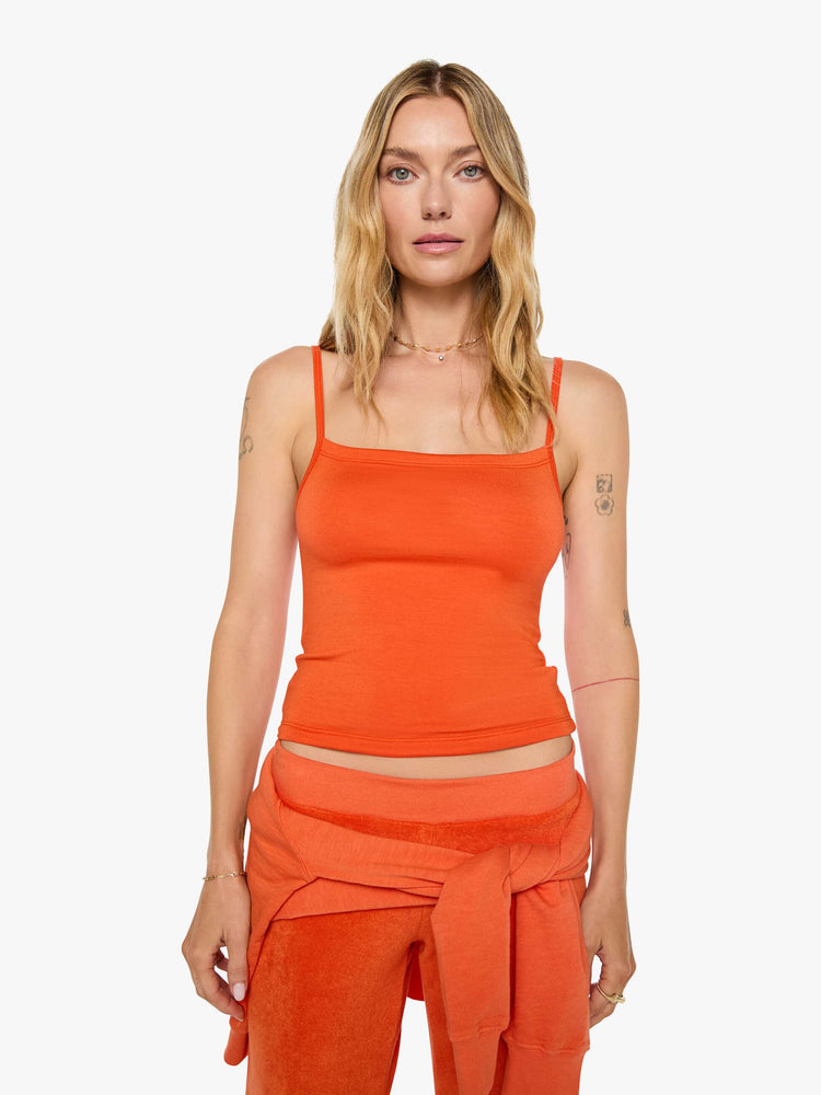 Front view of a woman in papaya orange tank designed with thin spaghetti straps, a scoop neck and cropped fit.