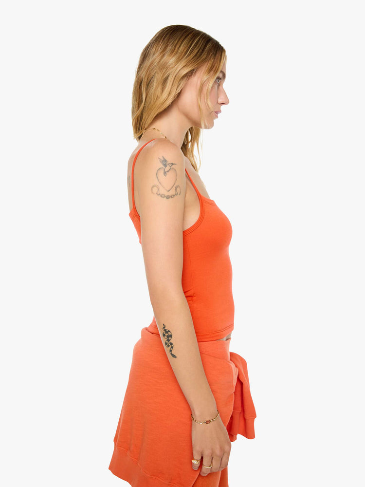 Side view of a woman in papaya orange tank designed with thin spaghetti straps, a scoop neck and cropped fit.