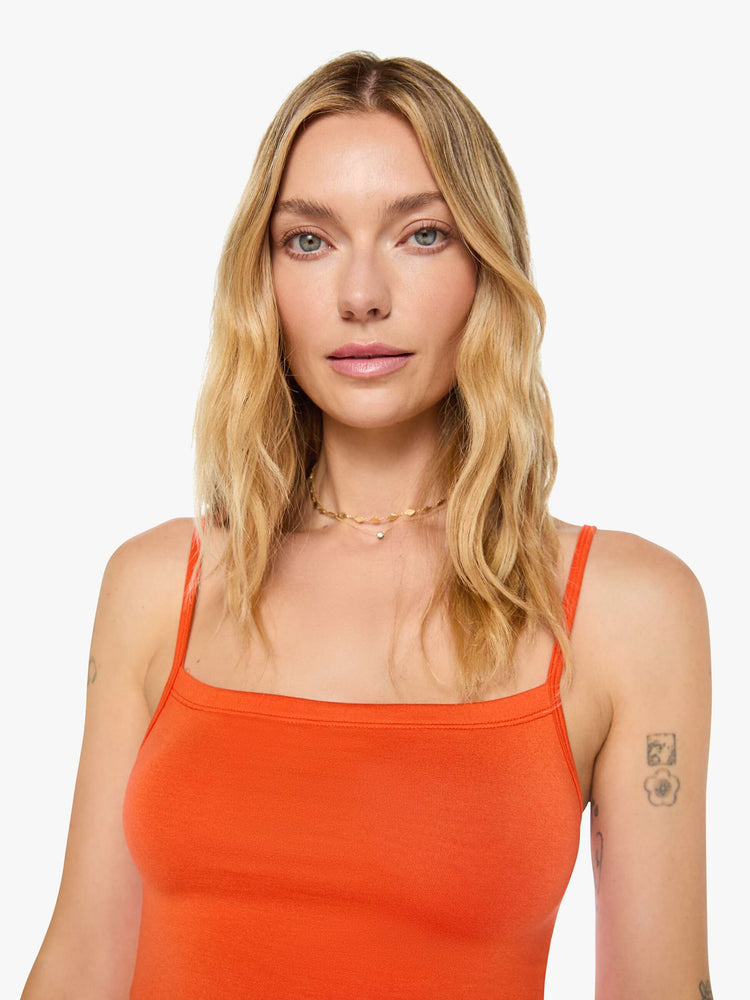 Close up view of a woman in papaya orange tank designed with thin spaghetti straps, a scoop neck and cropped fit.