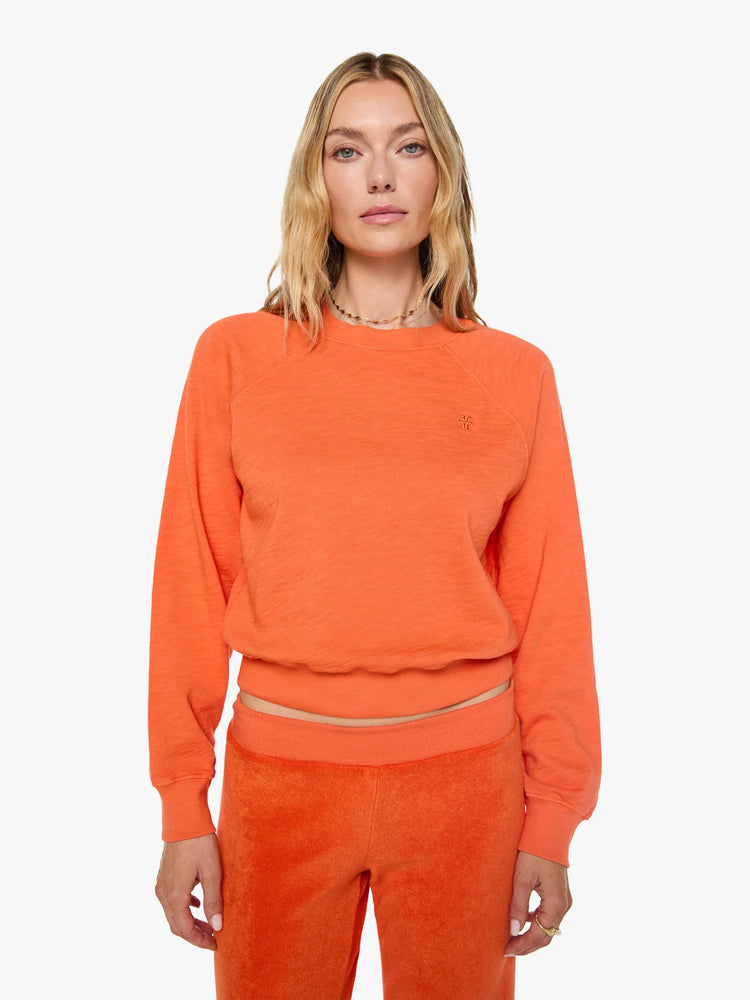 Front view of a woman in a  papaya orange raglan sweatshirt is designed with a crewneck, ribbed hems and a cozy fit.