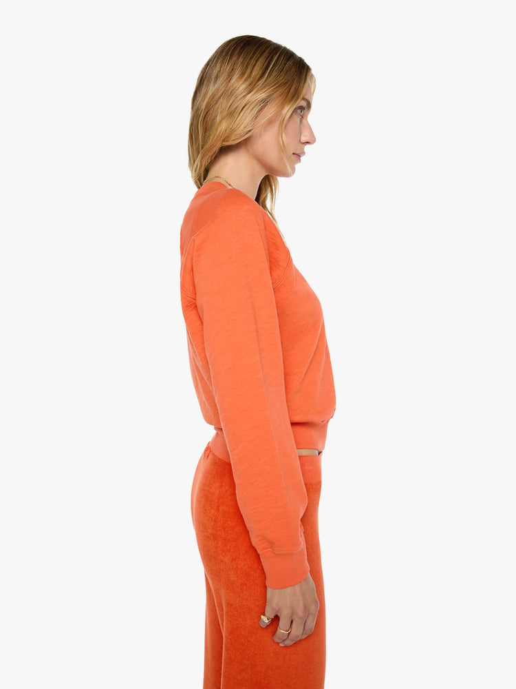 Side view of a woman in a  papaya orange raglan sweatshirt is designed with a crewneck, ribbed hems and a cozy fit.
