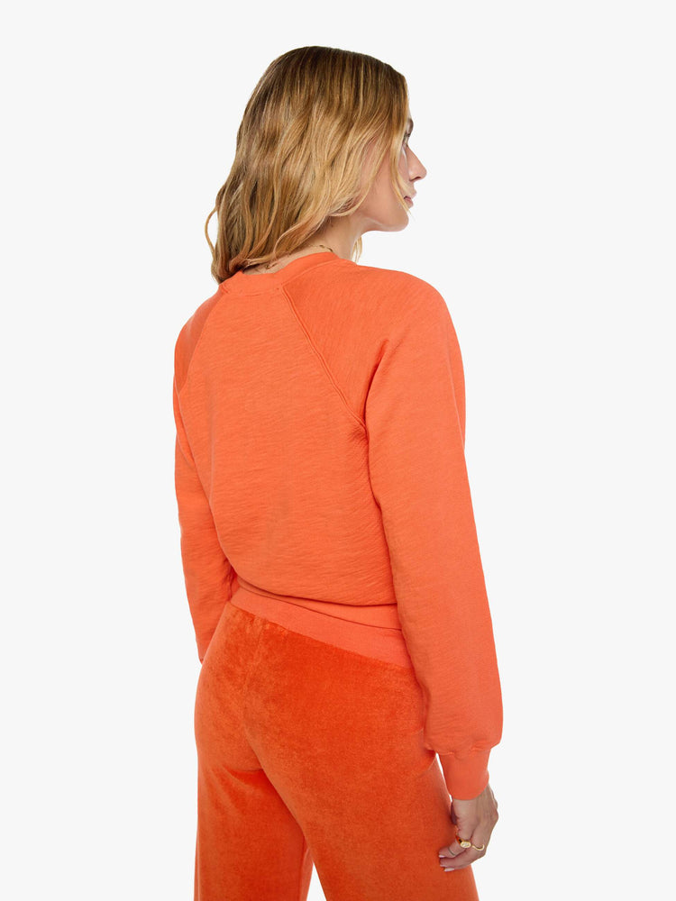 Back view of a woman in a  papaya orange raglan sweatshirt is designed with a crewneck, ribbed hems and a cozy fit.