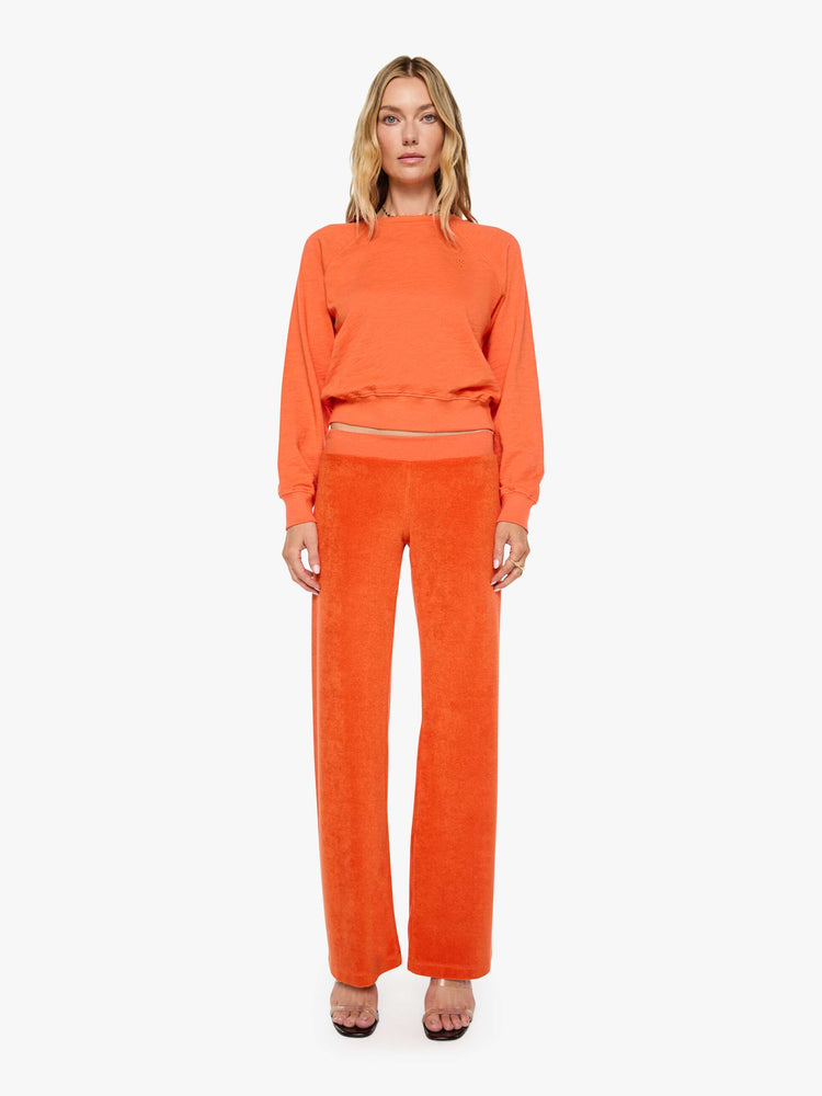 Full body view of a woman in a  papaya orange raglan sweatshirt is designed with a crewneck, ribbed hems and a cozy fit.