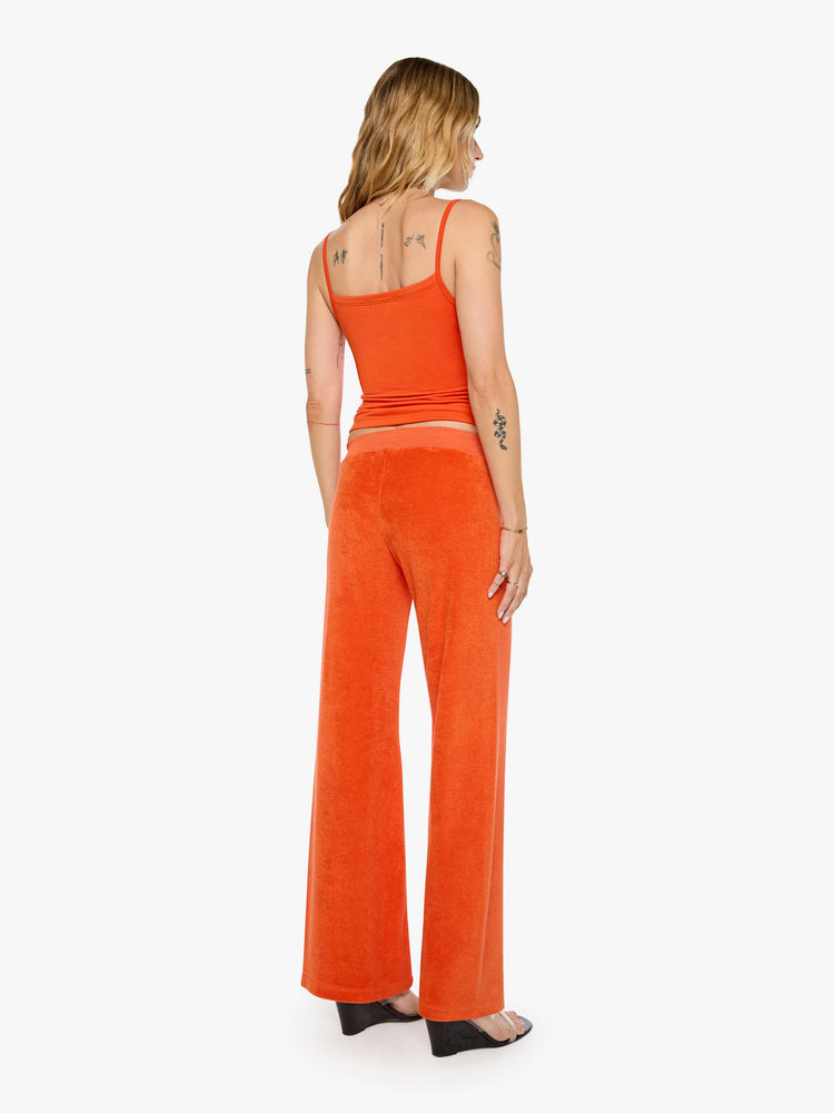 Back view of a woman in a papaya orange pants with a low rise, elastic waistband, loose leg and a cozy fit.