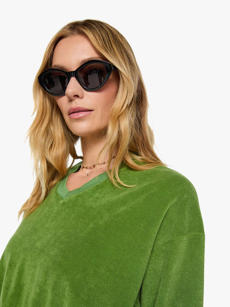 Close up view of a woman in a green sweatshirt is designed with a short V-neck, drop shoulders, ribbed hems and a cropped, cozy fit.