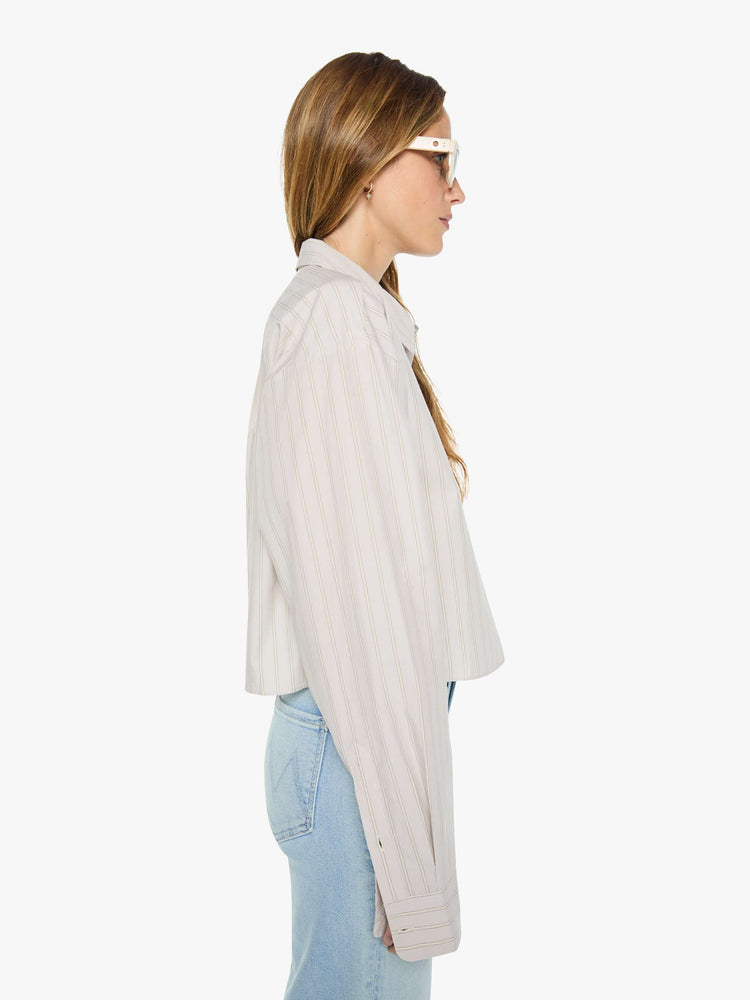 Side view of a woman in a grey with cream stripes button up top designed with a cropped, boxy fit. 