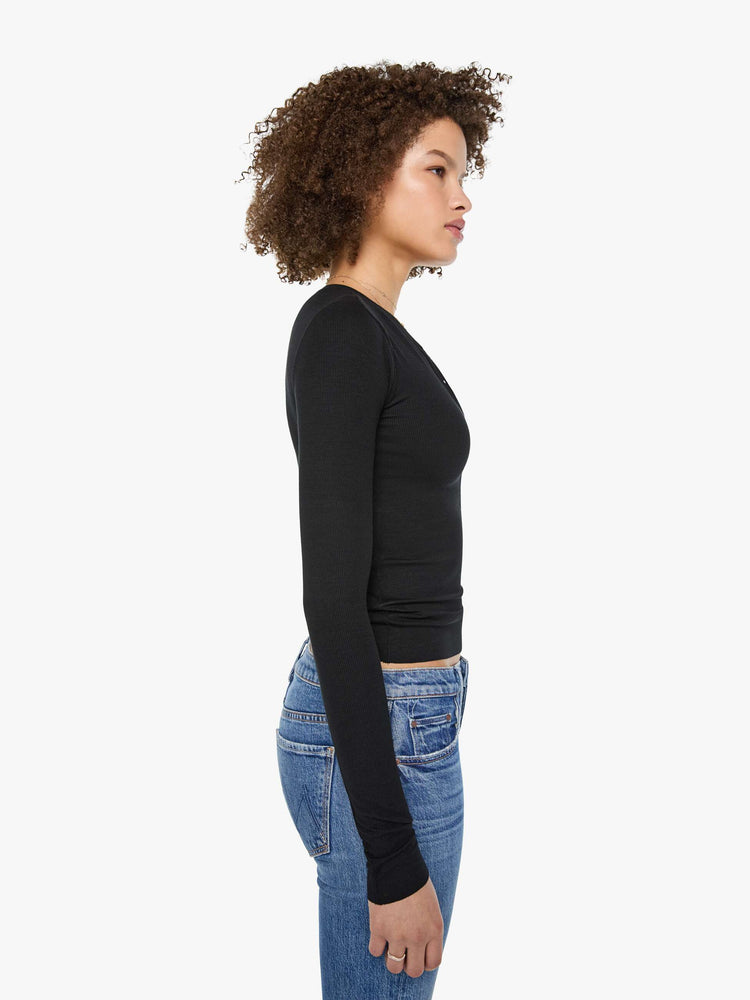 Side view of a woman in a  black with white buttons, the top is designed with a buttoned V-neck, long sleeves and a narrow fit.