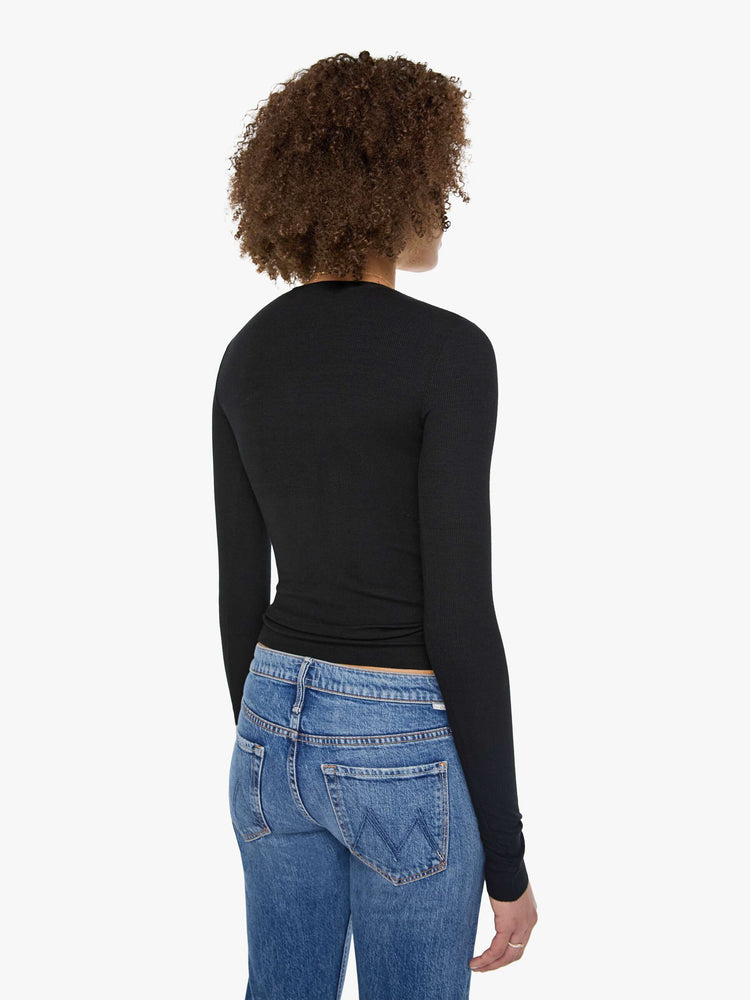 Back view of a woman in a  black with white buttons, the top is designed with a buttoned V-neck, long sleeves and a narrow fit.