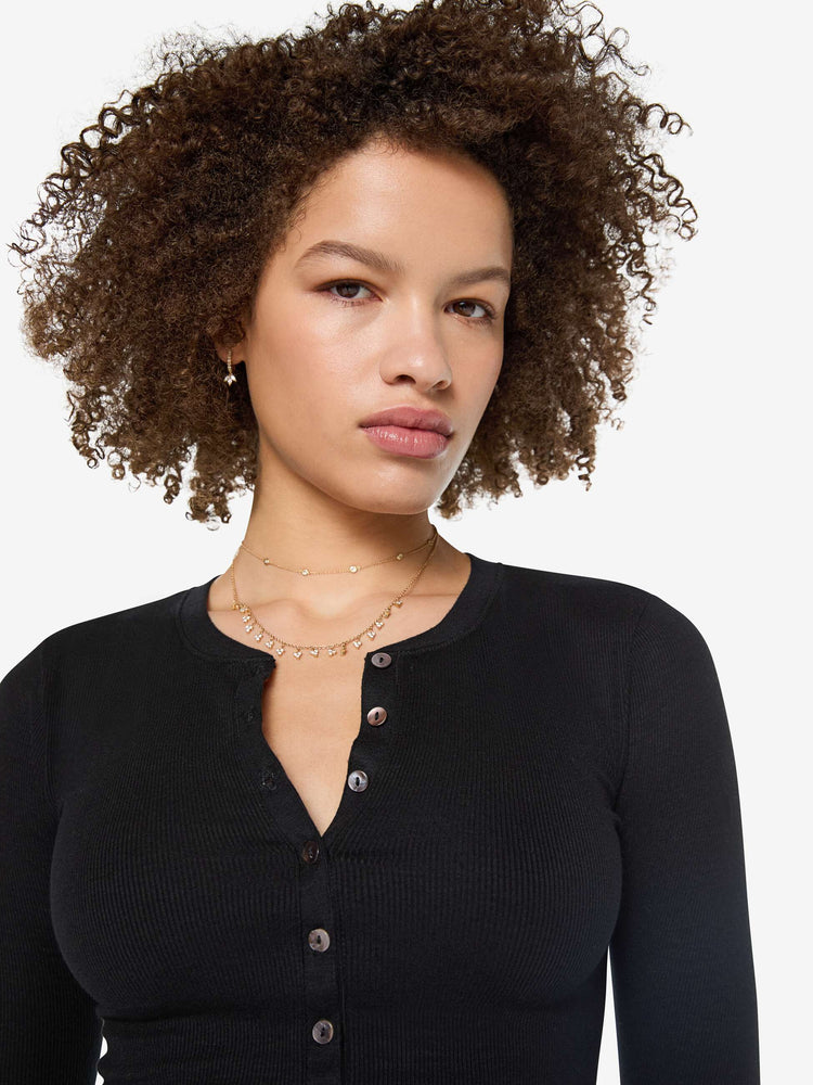 Close up view of a woman in a  black with white buttons, the top is designed with a buttoned V-neck, long sleeves and a narrow fit.