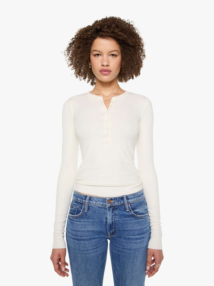 Front view of a woman in a cream with tonal buttons, the top is designed with a buttoned V-neck, long sleeves and a narrow fit.