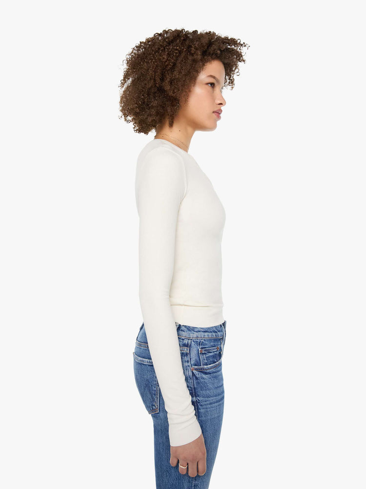 Side view of a woman in a cream with tonal buttons, the top is designed with a buttoned V-neck, long sleeves and a narrow fit.
