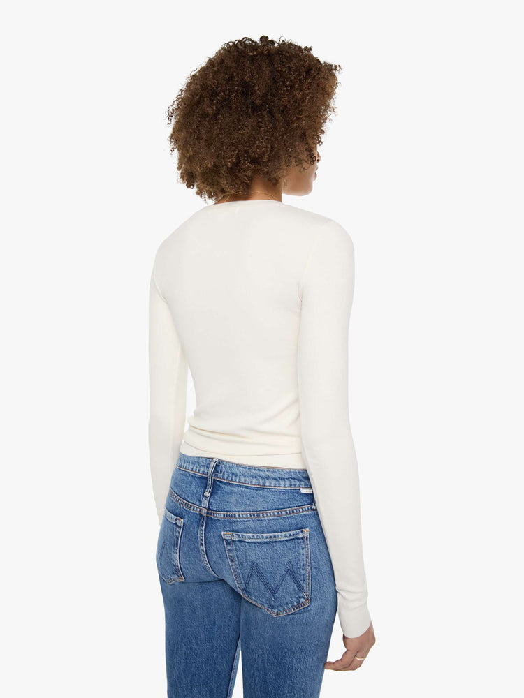 Back view of a woman in a cream with tonal buttons, the top is designed with a buttoned V-neck, long sleeves and a narrow fit.