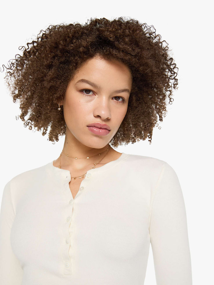 Close up view of a woman in a cream with tonal buttons, the top is designed with a buttoned V-neck, long sleeves and a narrow fit.