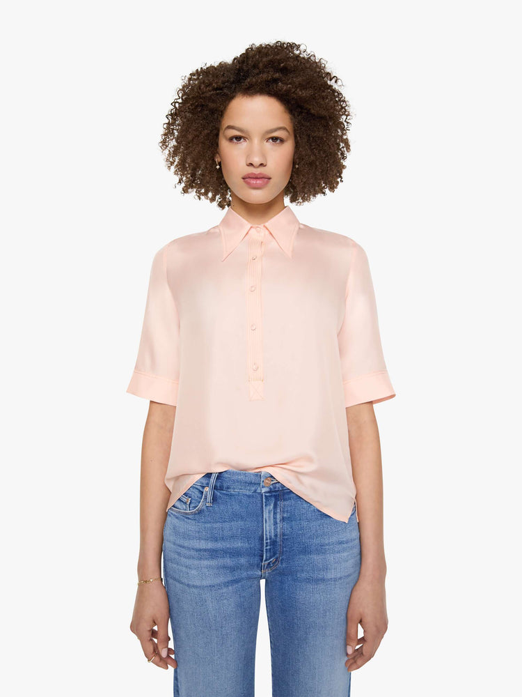 Front view of a woman in a light rose pink shirt with a collared neckline with an extra-long button placket, elbow-length short sleeves and a loose, boxy fit.