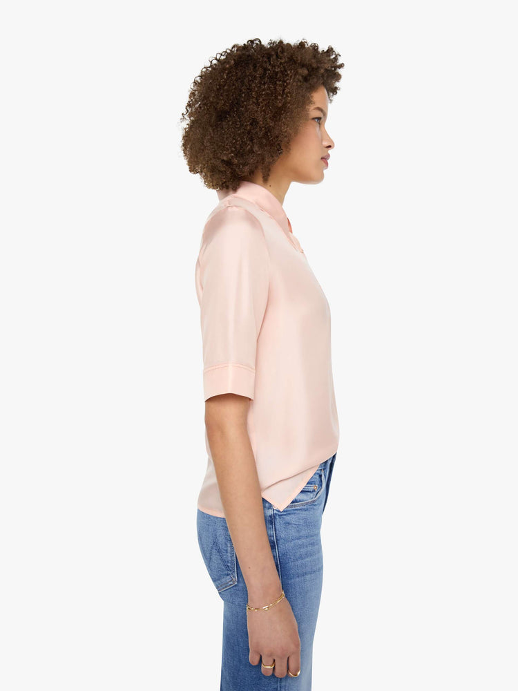 Side view of a woman in a light rose pink shirt with a collared neckline with an extra-long button placket, elbow-length short sleeves and a loose, boxy fit.