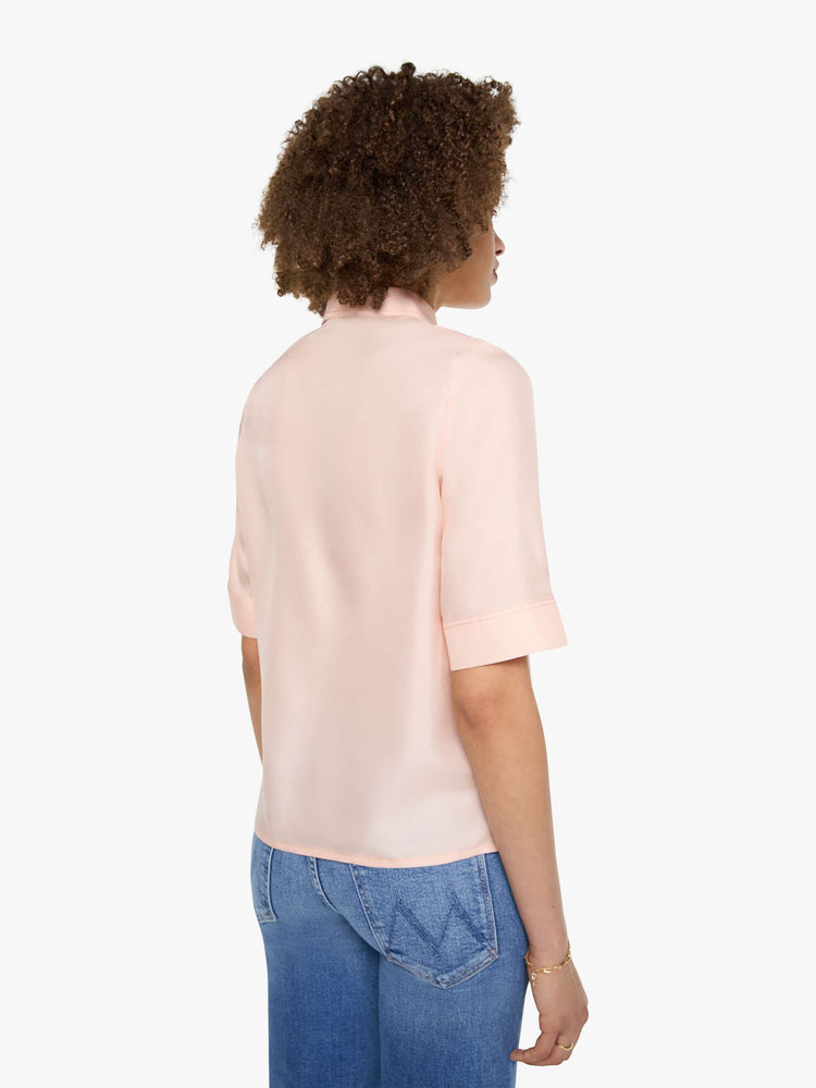 Back view of a woman in a light rose pink shirt with a collared neckline with an extra-long button placket, elbow-length short sleeves and a loose, boxy fit.