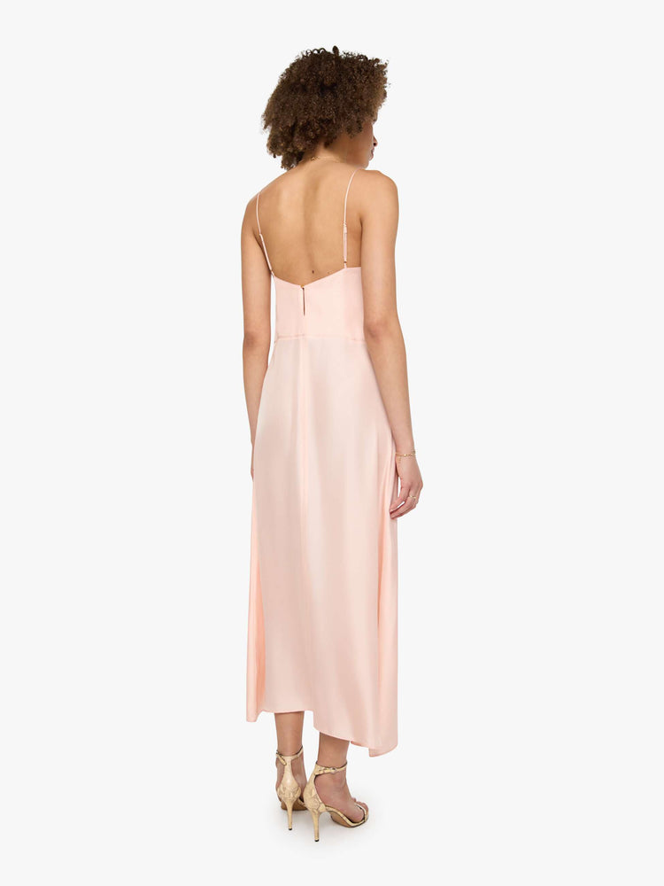 Back view of a woman in a light rose pink dress with thin spaghetti straps, a curved V-neck, a loose, flowy skirt and an ankle-length hem.