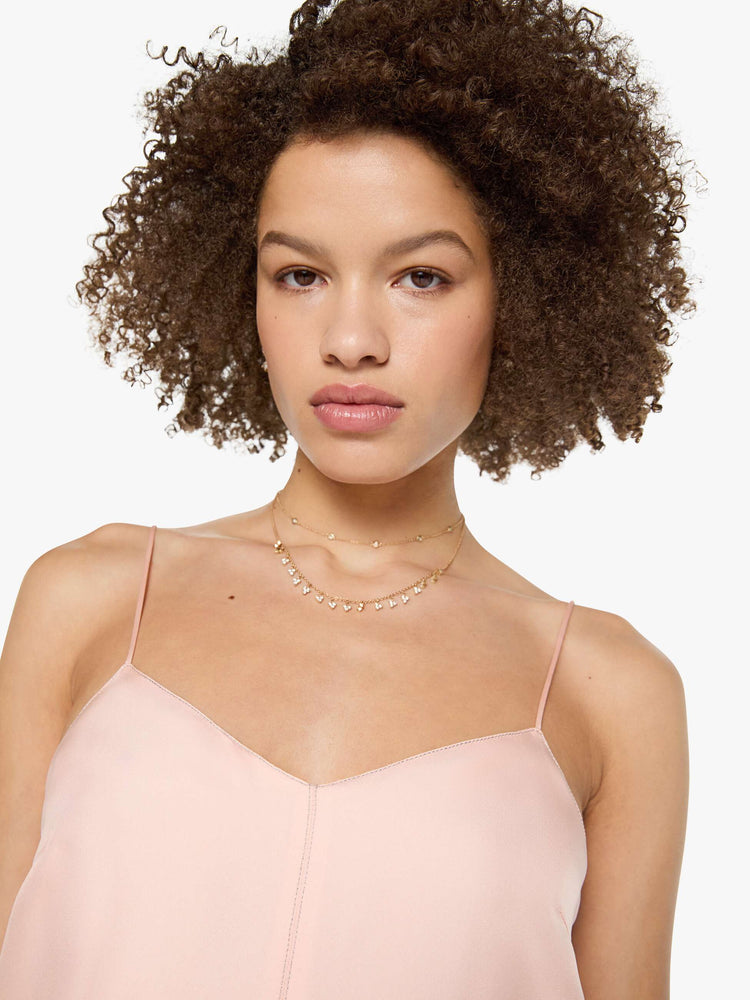 Close up view of a woman in a light rose pink dress with thin spaghetti straps, a curved V-neck, a loose, flowy skirt and an ankle-length hem.