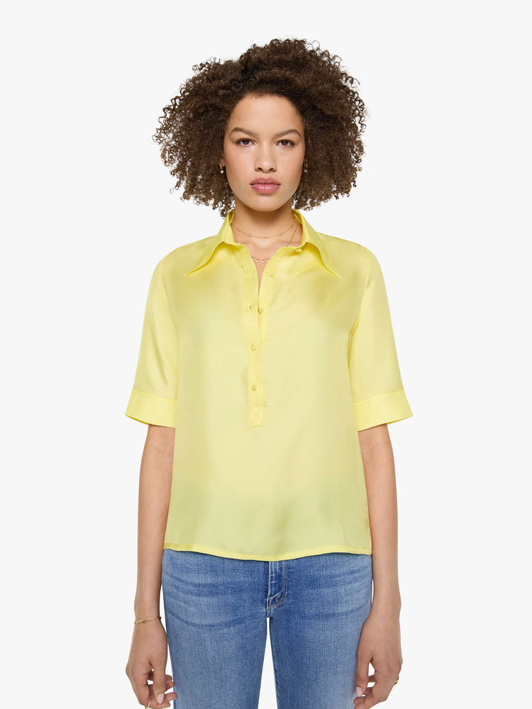 Front view of a woman in a light yellow shirt with collared neckline with an extra-long button placket, elbow-length short sleeves and a loose, boxy fit.