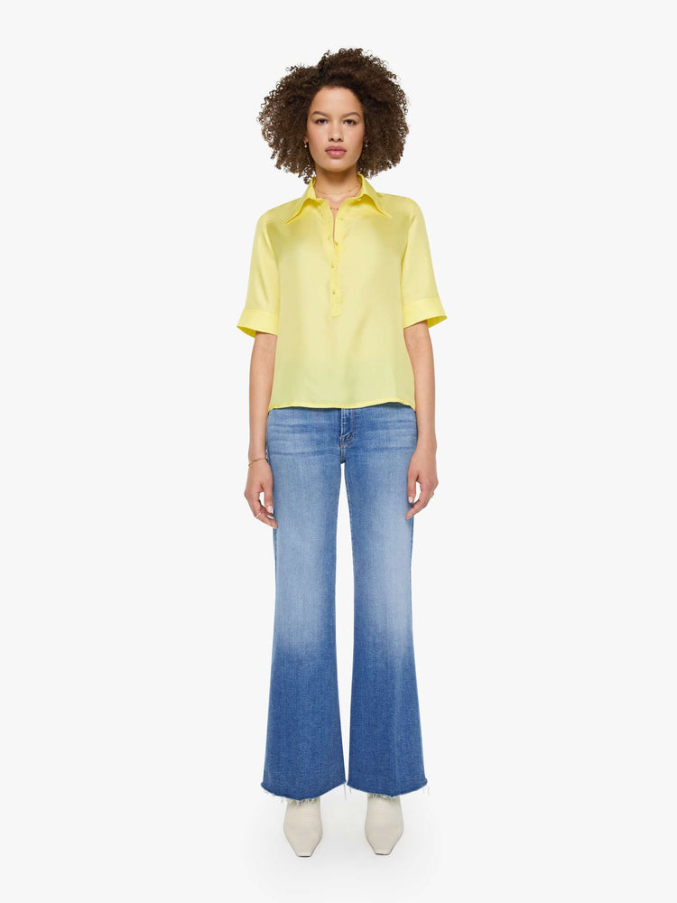 Full body view of a woman in a light yellow shirt with collared neckline with an extra-long button placket, elbow-length short sleeves and a loose, boxy fit.