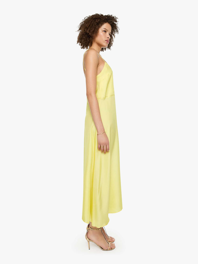 Side view of a woman in a light yellow, and features thin spaghetti straps, a curved V-neck, a loose, flowy skirt and an ankle-length hem.