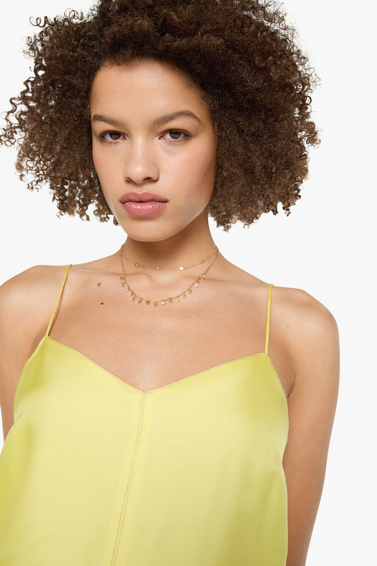 Close up view of a woman in a light yellow, and features thin spaghetti straps, a curved V-neck, a loose, flowy skirt and an ankle-length hem.