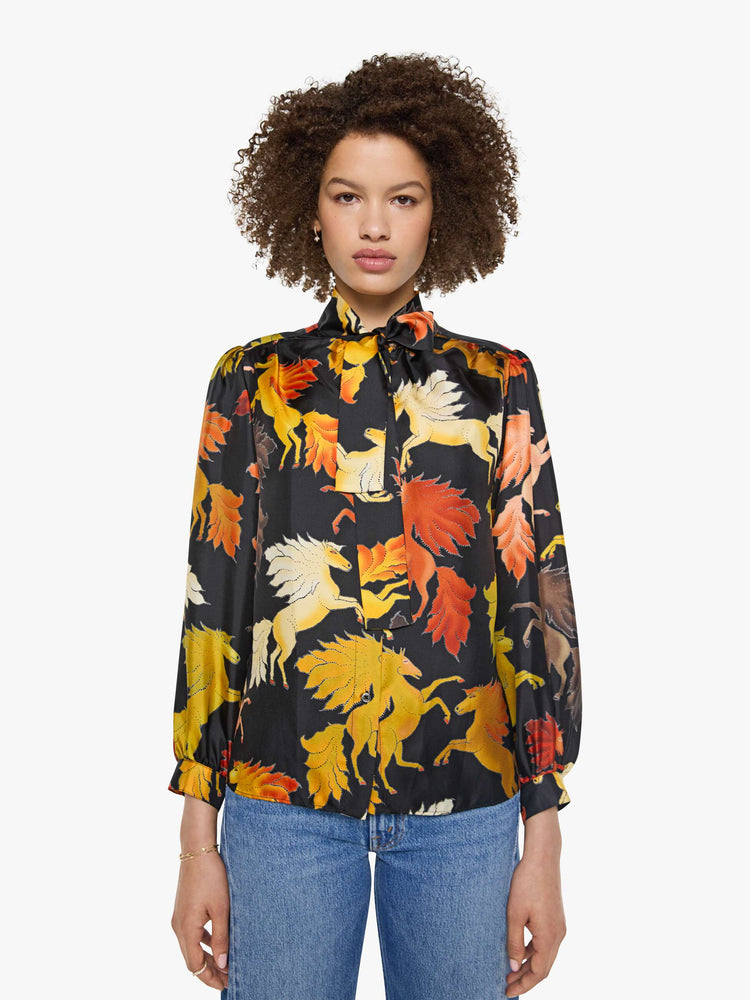 Front view of a woman in a black with a warm-toned horse print long sleeve blouse.