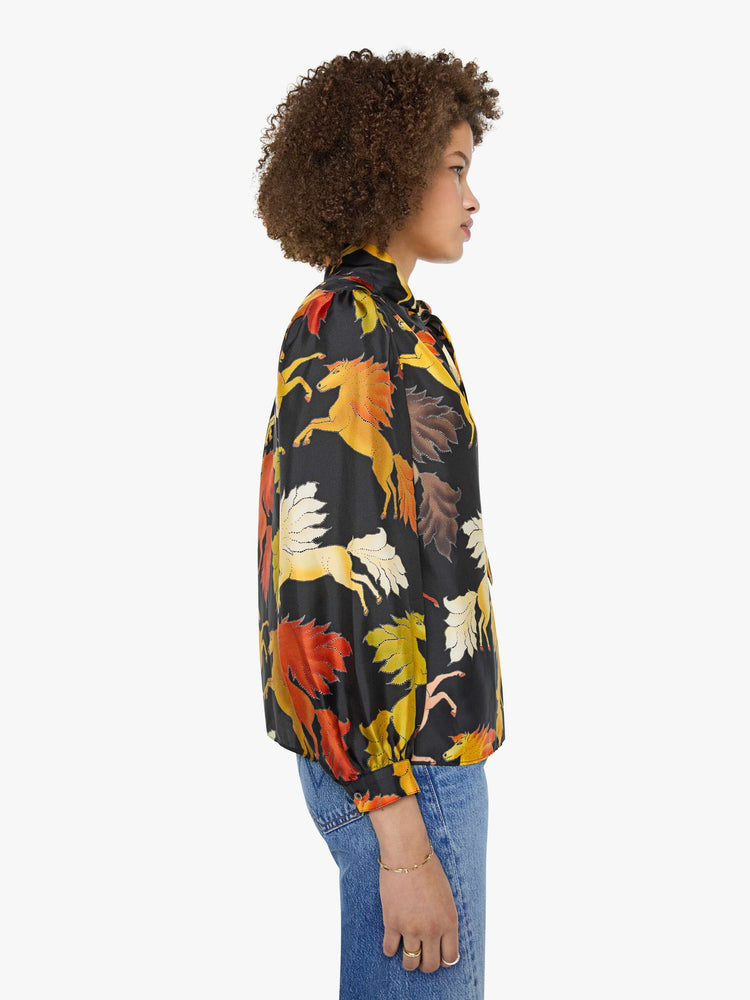Side view of a woman in a black with a warm-toned horse print long sleeve blouse.
