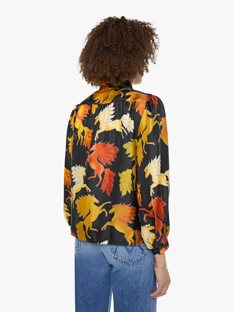 Back view of a woman in a black with a warm-toned horse print long sleeve blouse.