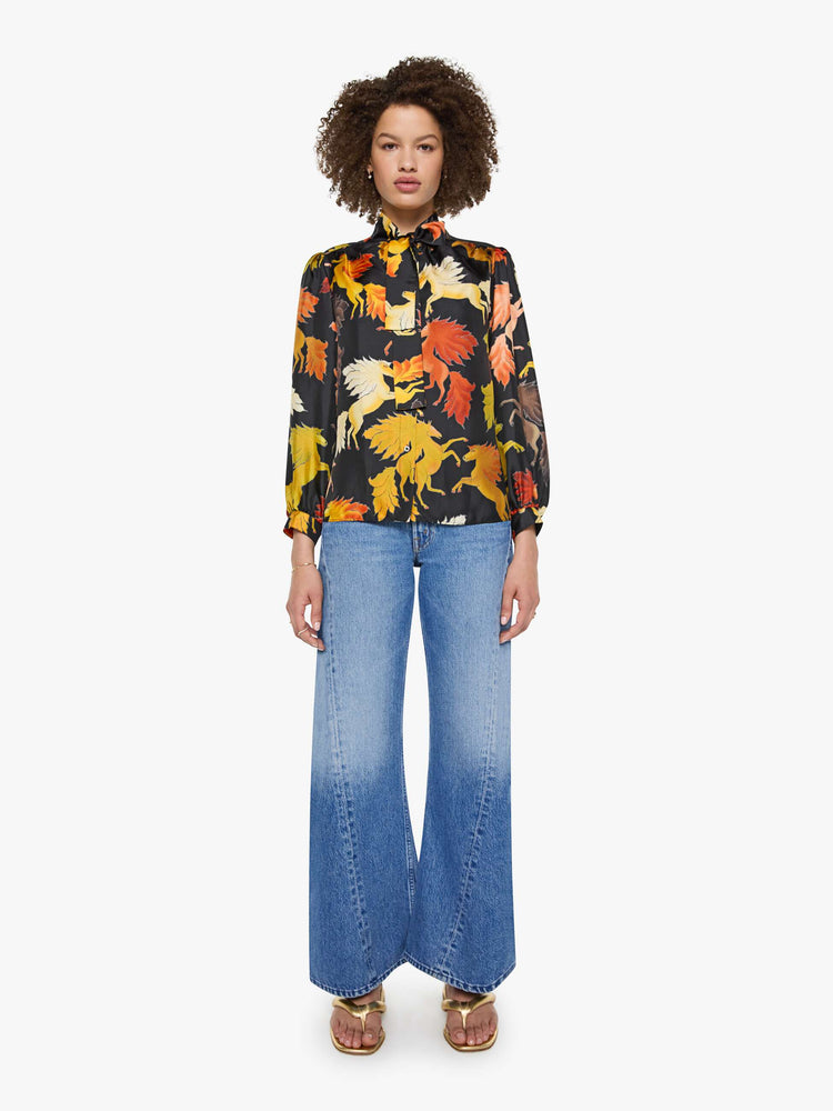 Full body view of a woman in a black with a warm-toned horse print long sleeve blouse.