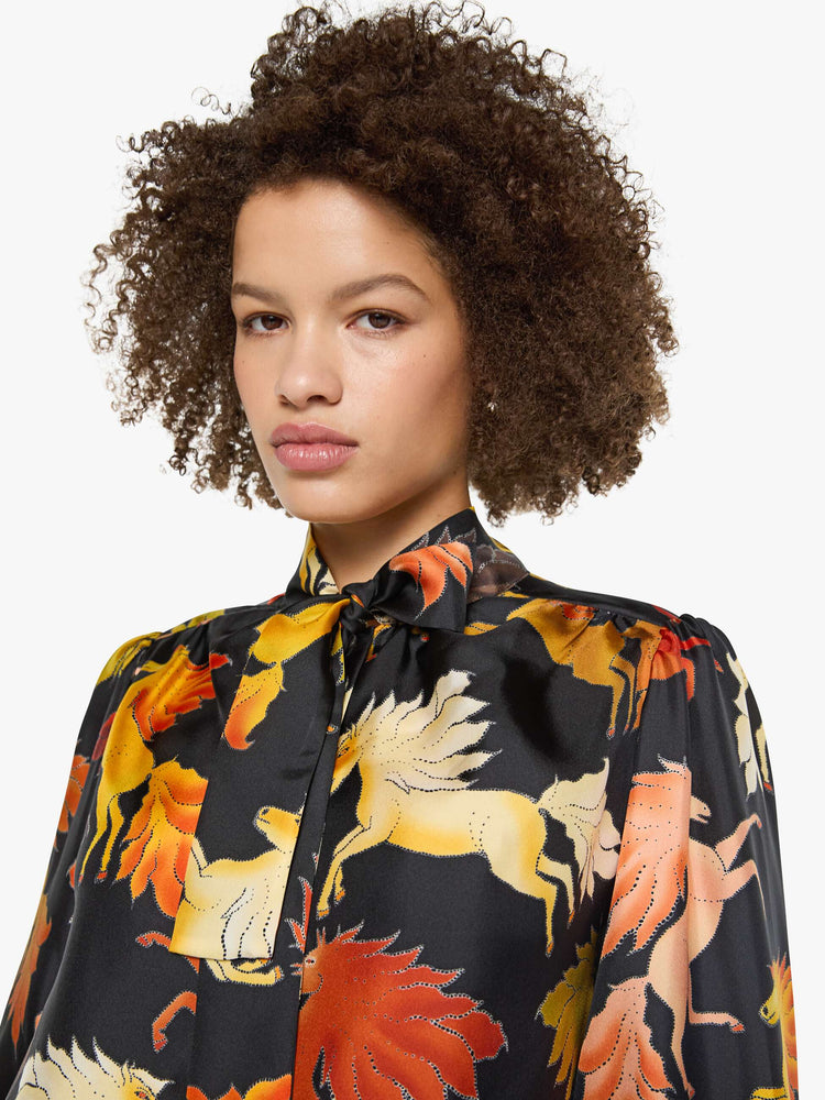 Close up view of a woman in a black with a warm-toned horse print long sleeve blouse.